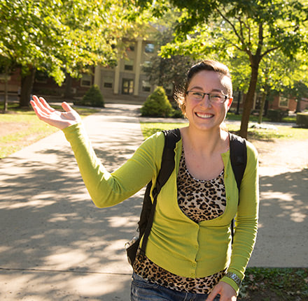 Student waving while walking across the Quad